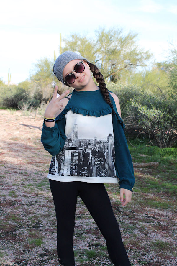 The cold shoulder Lynx with narrow ruffle along the yoke and long sleeves with button closure option. High neckline with tie closure.