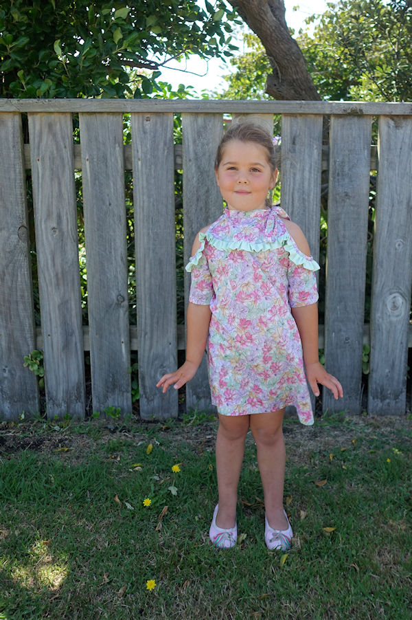 The cold shoulder Lynx dress with narrow ruffle along yoke and mid length sleeves. High neckline with tie on one side.