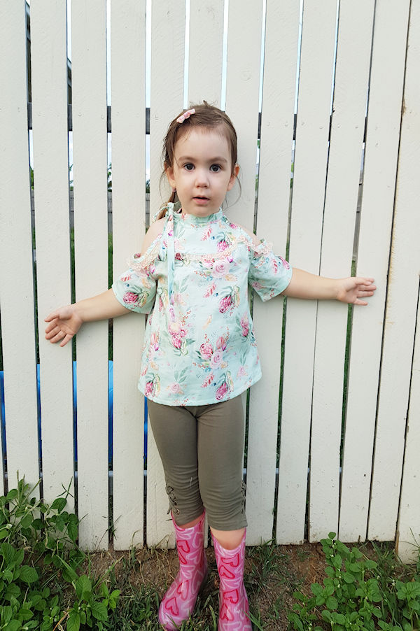 The cold shoulder Lynx dress with lace along yoke and shoulder opening. Mid length sleeves. High neckline with tie on one side.