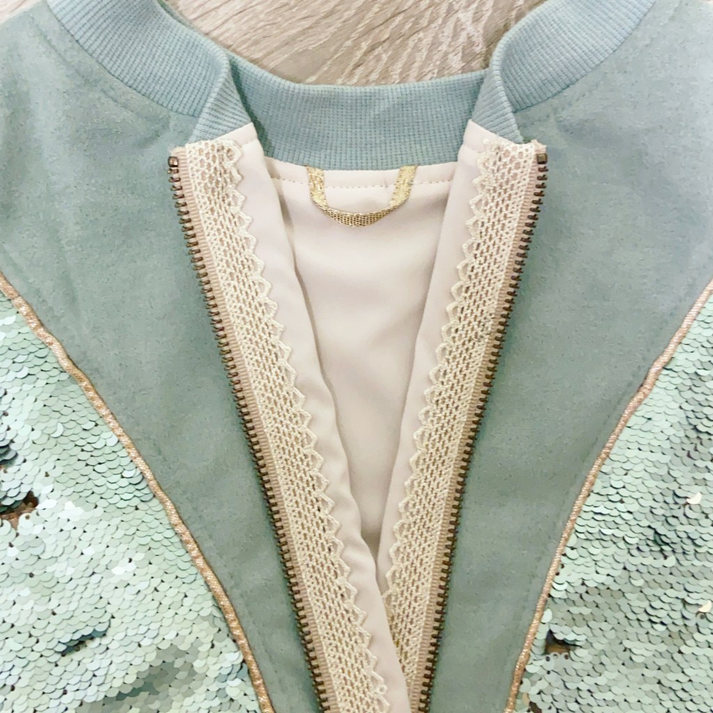 The inside of the Rose Hip bomber jacket with a hanging loop and gorgeous trim over the zipper tape.