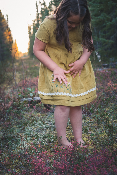 Young girl showing off the hand embroidery on a linen dress called Haze by Sofiona Designs.