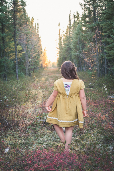 Young girl standing in the woods wearing a linen dress called Haze by Sofiona Designs.